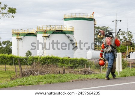 refinery tanks in the field with a lawn mower worker