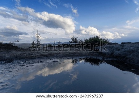 Reflecting clouds in a puddle along with the surrounding mountains. Stolowe Mountains, Klodzka Valley, Lower Silesia Voivodeship