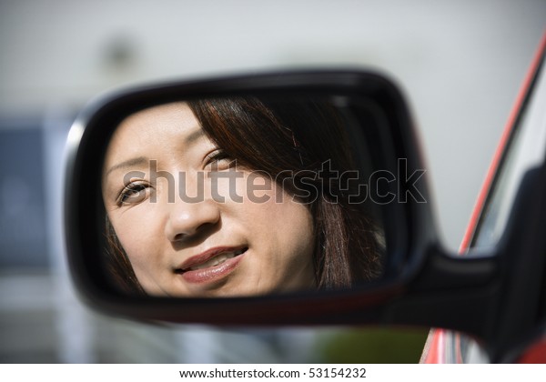 Reflection of Asian woman in side  view car\
mirror smiling.