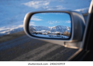 reflection of a beautiful winter landscape with mountains and village in the snow in rearview mirror of the car. The concept of festive holiday winter travel - Powered by Shutterstock