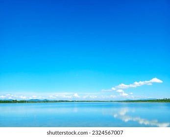 reflection of blue sky and white cloud on lake surface with line of tree and tiny hill - Powered by Shutterstock