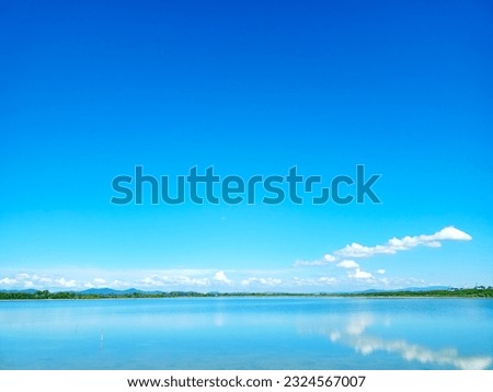 reflection of blue sky and white cloud on lake surface with line of tree and tiny hill