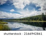 Reflection of blue sky with white clouds in the mirror surface of mountain lake. Beautiful Alpine natural landscape.