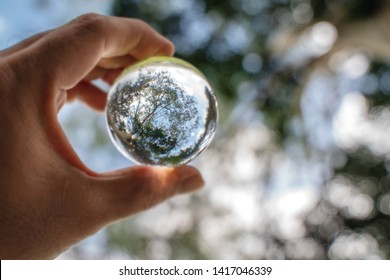 Reflection of blue sky, white clouds and trees in a glass ball in holding hand