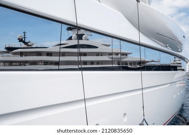 Reflection of a boat on a glossy surface of a huge yacht at sunny day, the chrome plated handrail, megayacht is moored in port