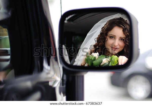 reflection of the bride\'s face in the rearview mirror\
in the car