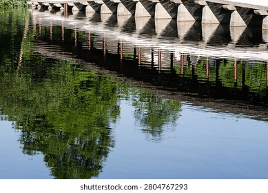 A reflection of a bridge and lush green trees on calm water, capturing symmetry and tranquility in a natural setting.