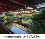 Reflection of a Bridge under it on the river Lea going from Stratford to Hackney Marsh. Strong metal structure. Afternoon walk in a sunny summer day for exercise. Lots of plants, trees and shrubs.