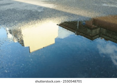 Reflection of a building in a puddle of water. The reflection is distorted and blurry, giving the impression of a dreamlike or surreal scene