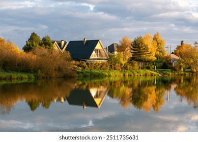 Reflection in the calm water of the pond of the autumn forest and the triangular modern house in the village - Powered by Shutterstock