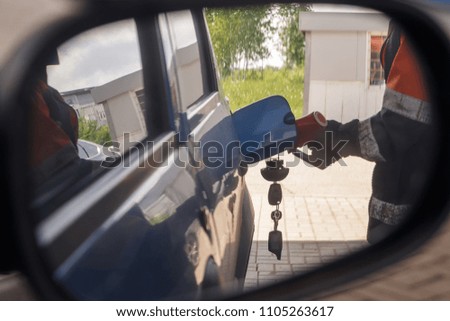 Reflection in car mirror of the man fuel the car on petrol stati