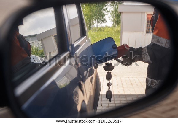 Reflection in car mirror of the man fuel the car on\
petrol stati