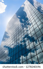 Reflection of clouds and blue sky on glass windows wall of office building with sun behind building