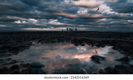 Reflection of a dramatic cloudy sky in the water on the rough stone surface of an old pier. Seagull in the sky and fishermen on a blurred background - Powered by Shutterstock