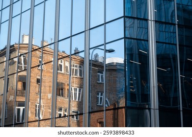 Reflection of the facade of an old brick abandoned residential building in the glass facade of a modern office building