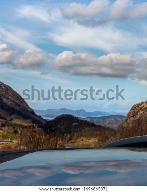 Reflection of floating clouds across the sky on the\
roof of a car