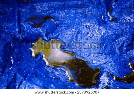 The reflection of a forest canopy on a pool of dirty rainwater collected in a blue canvas tarp