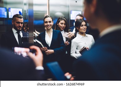 Reflection Of Group Of Amused Smiling People In Suits Carrying Documents And Taking Pictures With Smartphone While Standing Together In Elevator Cabin At Urban Office Building