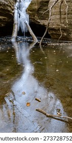 A reflection of an icefall and the sky is shown on the ice of the Icefall splaskpool, Kaskaskia Canyon, Starved Rock State Park, LaSalle County, Illinois