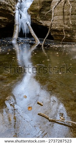 A reflection of an icefall and the sky is shown on the ice of the Icefall splaskpool, Kaskaskia Canyon, Starved Rock State Park, LaSalle County, Illinois