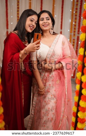 Reflection of Indian women posing for a selfie in the mirror on the occasion of Diwali. Beautiful Indian sisters posing for the camera in a decorated house for the celebration of Deepawali