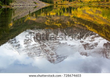 Reflection of Maroon Peak on Maroon Lake and aspen trees with its gold yellow leaves in fall foliage autumn season in a bright day light sunny day cloudy blue sky, Aspen, Colorado, USA.