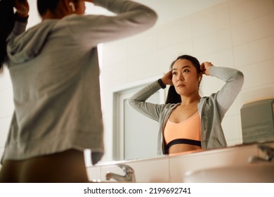 Reflection in a mirror of Asian sportswoman tying  up her hair at gym's bathroom.  - Powered by Shutterstock