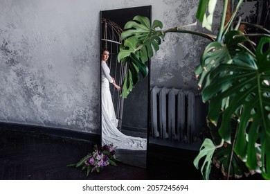 Reflection in the mirror of a bride in an iron cage on a gray concrete background. Patriarchal marriage concept. Unhappy, fashion young woman trying to break free through the bars. Fictitious marriage