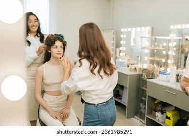 Reflection in mirror of creating creative image for photoshoot. Female makeup artist and hairdresser getting ready female to event wedding or important meeting. Four-handed makeup and styling concept. - Powered by Shutterstock