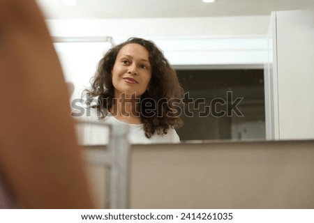 Reflection in the mirror of a smiling happy woman admiring her appearance in the bathroom mirror. Home spam beauty, body and skin care concept. Ageing process. Selective focus