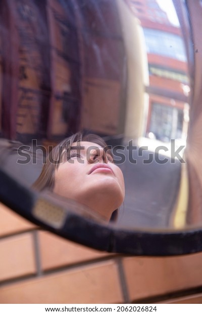 Reflection in the mirror of white european woman\
outside in an industrial\
area