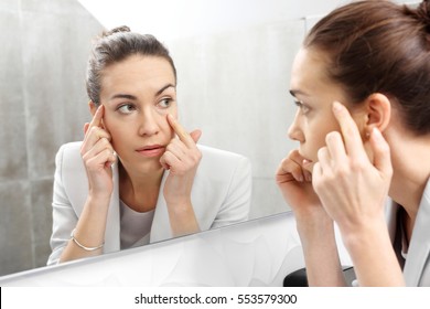 Spiegelreflexion.
Frau schaut im Spiegel auf die ersten Falten.
