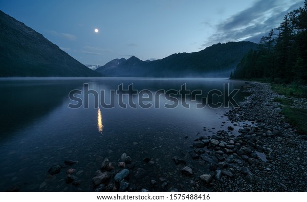 Reflection of the moon in a mysterious foggy lake.\
Wild russian nature. Beautiful landscape with lake in the\
mountains. Traveling in the Altai Republic. Active tourism in\
Russia. Multa Lake.