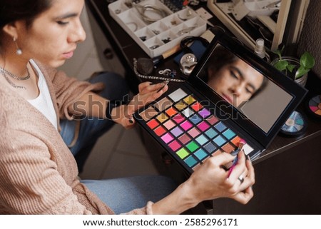 Reflection of a non-binary person in the mirror putting on makeup before going to work
