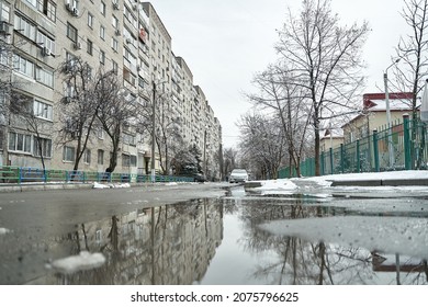 Reflection On The Puddle Of Winter Snow Covered City Scenery.