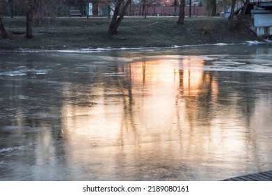 Reflection of orange sunset and trees in ice of frozen river in winter, abstraction