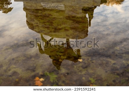 Reflection of people statue and fall foliage trees of retiro park in pool pond of monument man riding a horse people walking by the cement stone edge autumn sunset cloudy blue sky on sunny day Spain
