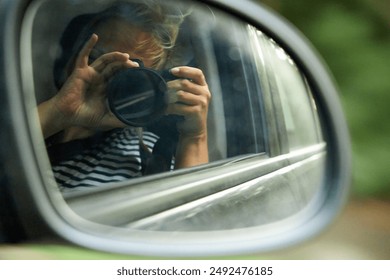 reflection of a person with a camera in the side mirror of a car