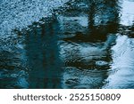 A reflection of a person in the water, with raindrops falling on the surface. Scene is calm and peaceful, as the rain creates a serene atmosphere