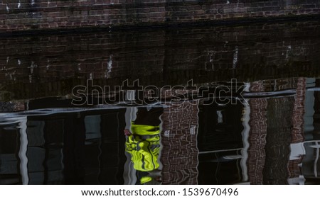 reflection of a person in a yellow jacket in the water of a canal