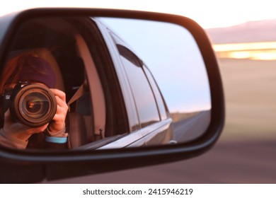 Reflection of a photographer taking a photo in the side mirror of a car during a sunset drive. - Powered by Shutterstock