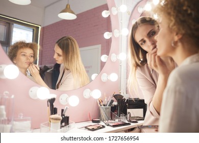 Reflection Portrait Of Young Woman Applying Make Up On Client By Vanity Mirror In Pink Dressing Room Interior, Copy Space