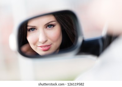 Reflection of pretty woman in the side-view mirror of the car that she took to have a little trip