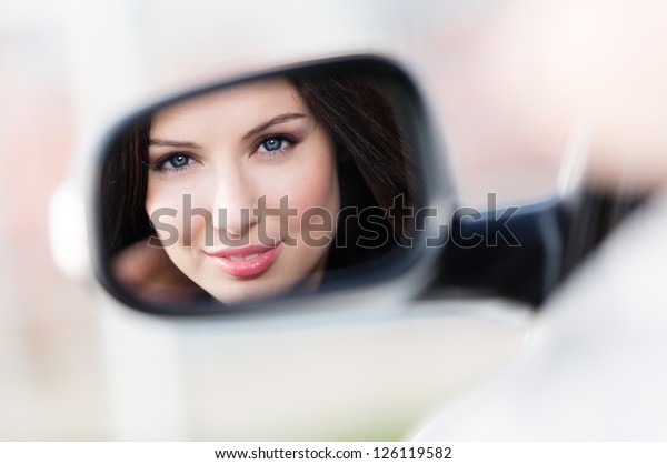 Reflection of pretty woman in the\
side-view mirror of the car that she took to have a little\
trip