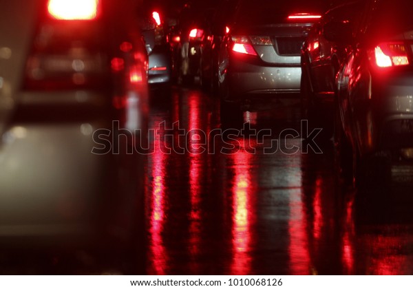 reflection of the red brake light on a wet\
road when the street is crowded at night\
time