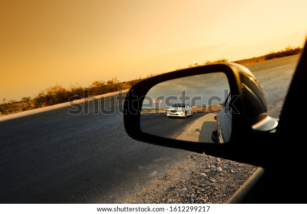 reflection in the side car rear view mirror of a\
white car traveling along the road at sunset. Design element,\
cover. Web banner.