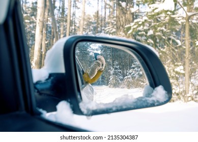 reflection in the side mirror of the car, women's hands in mittens taking pictures of the winter forest on the phone