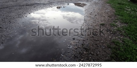 Reflection of the sky in puddle of water. Summer day after rain. White gray clouds float across the blue sky. The sky and clouds are reflected from the surface of a puddle of water on the gray ground.