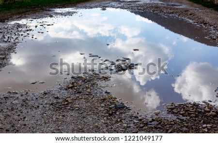 Reflection of sky sun  clouds in Puddles A silent and sandy road on a very bad condition This is a situation nowadays on public roads when the winter is coming. Road is filled with holes with water 