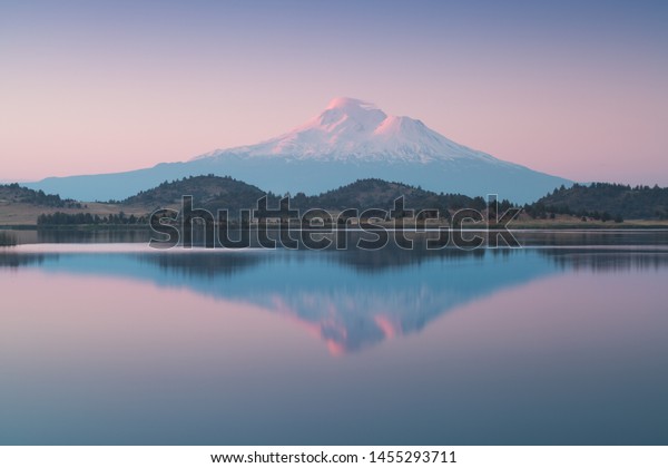 A reflection of snow capped Mount Shasta in a clear\
water in lake  at sunrise in California State, USA. \
Mount Shasta\
is a volcano at the southern end of the Cascade Range in Siskiyou\
County 